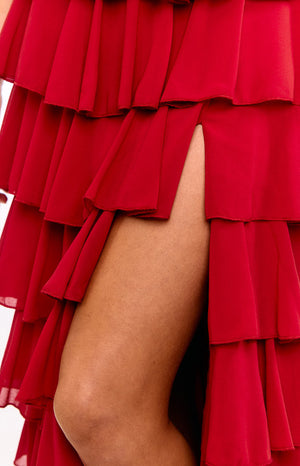 A model wears a vibrant red strapless maxi dress. This statement formal gown features a dramatic ruffle trim that cascades down with a leg split. A beautiful choice for a wedding guest or prom dress.