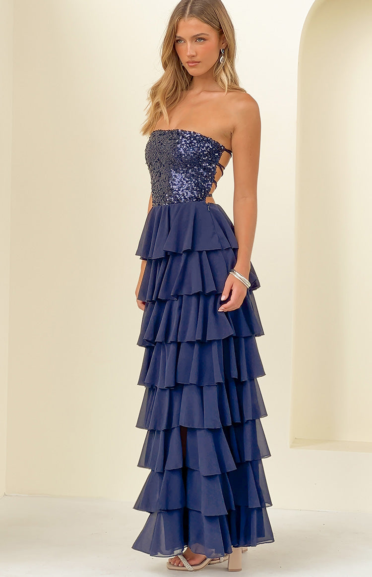 Side view of a navy strapless maxi dress with a sequin bodice, lace-up side cutouts, and a tiered ruffle skirt