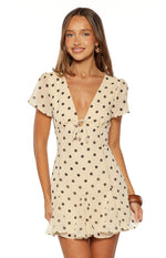Front view of a cream polka dot mini dress with a deep V-neck, ruched bust, and a front tie detail
