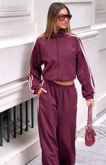 Cropped burgundy track jacket with a high neck, full zip front, and pink stripes down the long sleeves