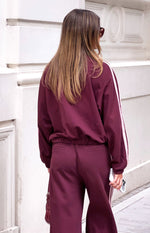 Rear view of a burgundy track jacket with an elasticated hem and pink stripes down the long sleeves