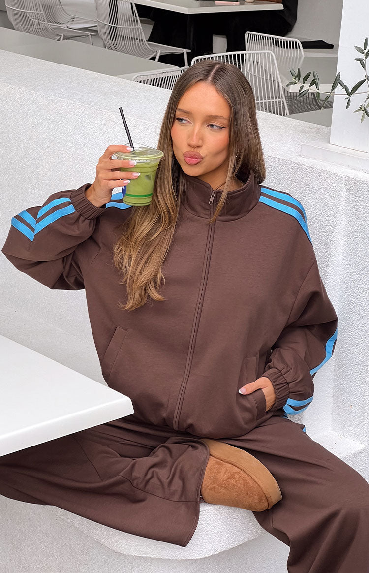 Front view of a chocolate brown zip-up jacket with a stand collar, blue stripes on the sleeves, and elasticated cuffs