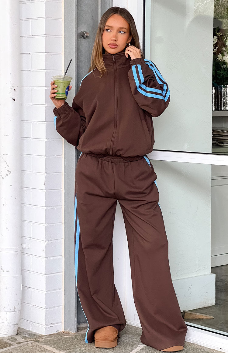 Full length view of a chocolate brown zip-up jacket with blue sleeve stripes and matching wide-leg pants with side stripes