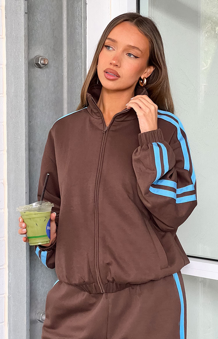 Close-up of the chocolate brown jacket showing the high zip-up collar and blue stripes on the sleeve