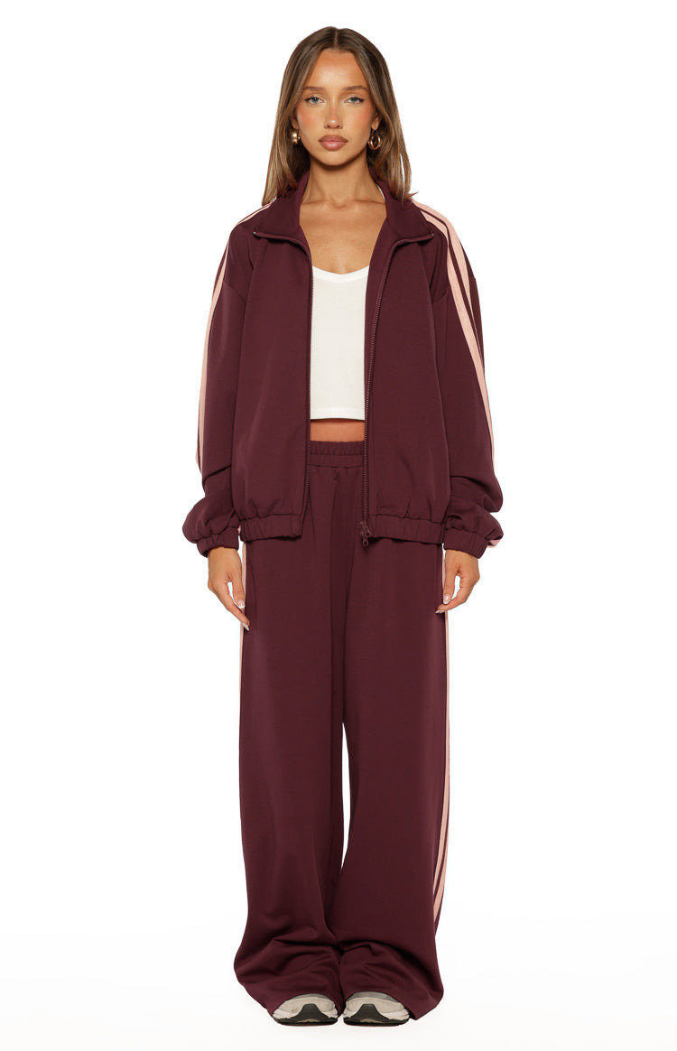 Front view of a relaxed fit burgundy track jacket with pink sleeve stripes, high collar, full zip, and elasticated hem