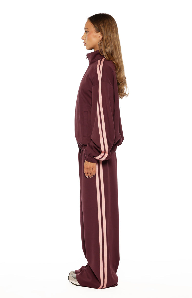 Side view of a burgundy track jacket with pink double stripes down the sleeves, showing the relaxed fit and high collar