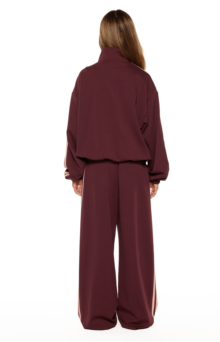 Rear view of a burgundy oversized track jacket with a high collar, long sleeves with pink stripes, and an elasticated hem