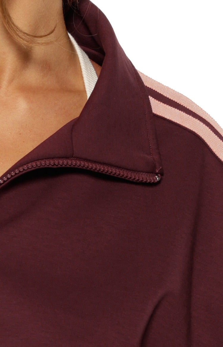Close-up of the burgundy track jacket's half-zip high collar and pink striped shoulder