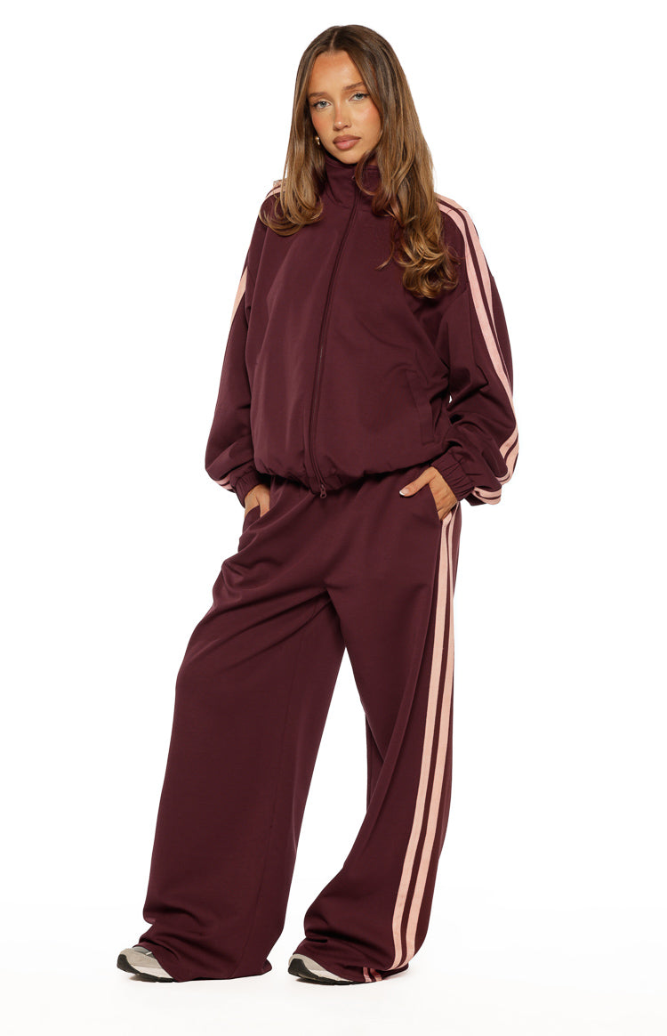 Full front view of a burgundy track jacket with a high collar and pink stripes on the sleeves, relaxed fit