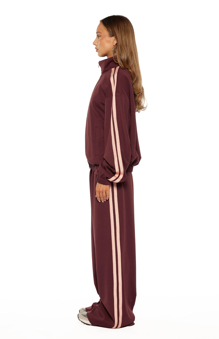 Side view of burgundy wide-leg track pants with pink side stripes, showing the full length and relaxed fit