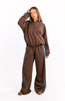 Full-length image of a person wearing a pair of brown wide-leg track pants with a light blue stripe down each side. Our pants have an elastic waistband and pockets best for your athletic mood.
