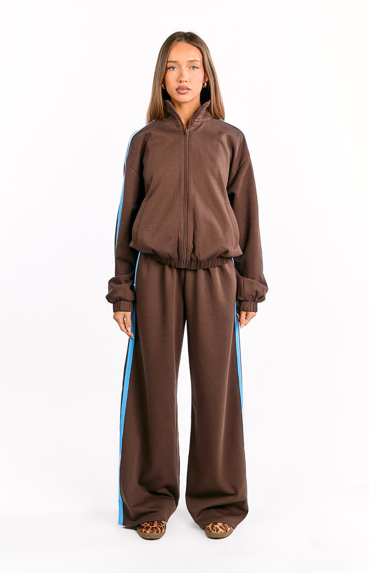 Front view of a chocolate brown zip-up jacket with a high collar and blue and black side stripes, worn with matching wide-leg pants