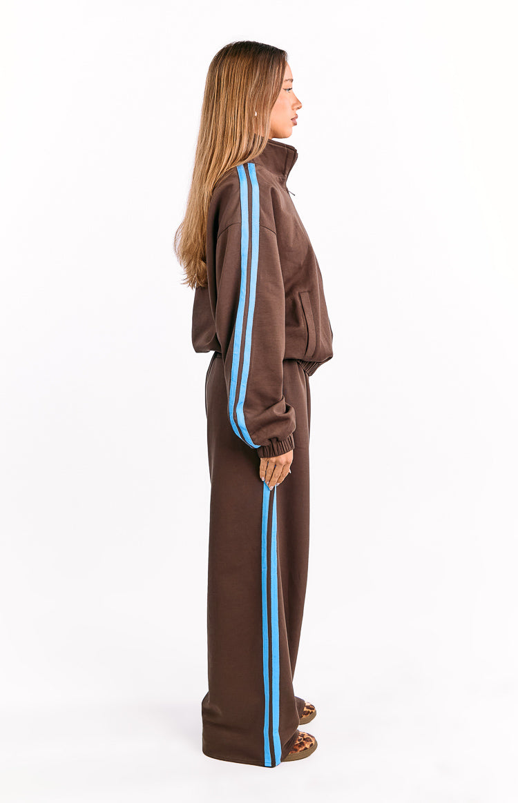 Side view of a chocolate brown relaxed fit jacket with blue sleeve stripes, high collar, ribbed cuffs, and side pockets