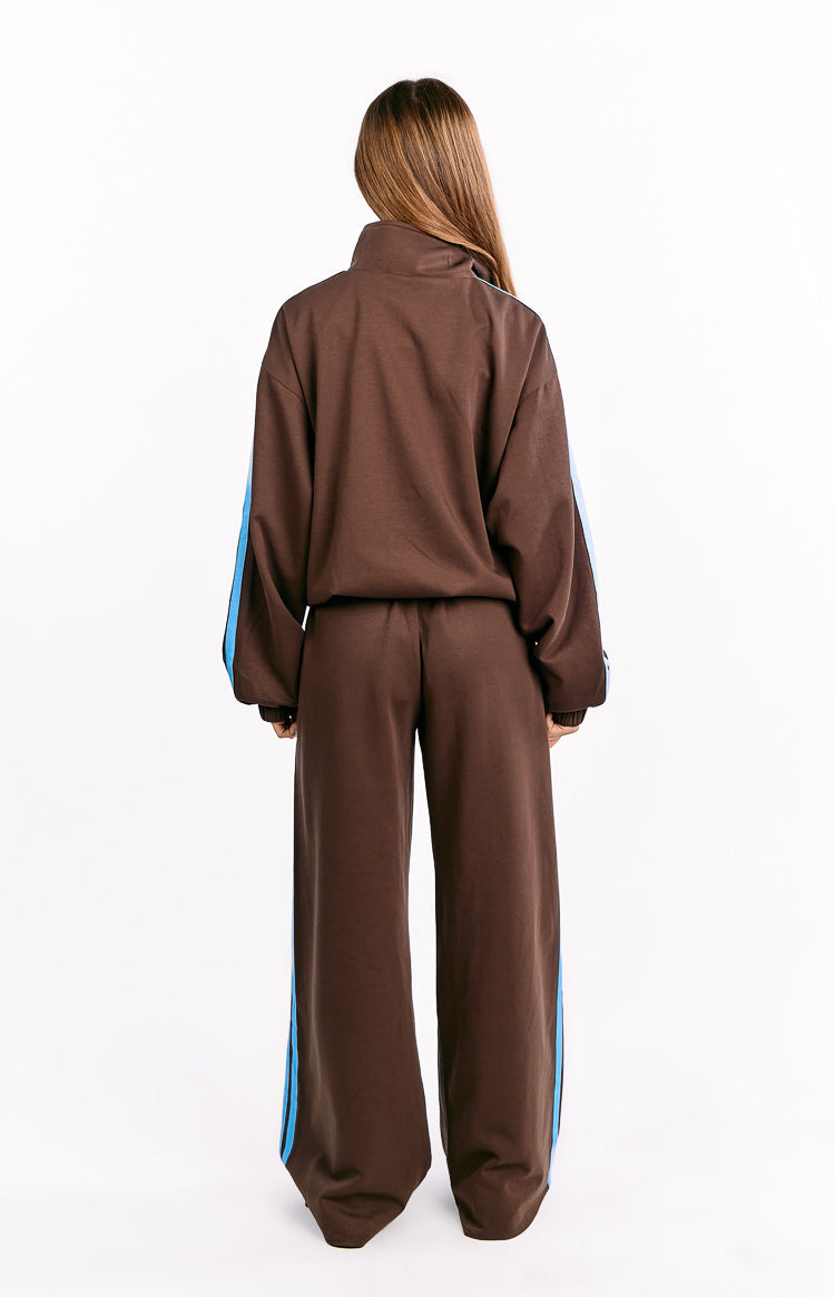 Rear view of a chocolate brown jacket with blue stripes on the sleeves, paired with matching wide-leg pants