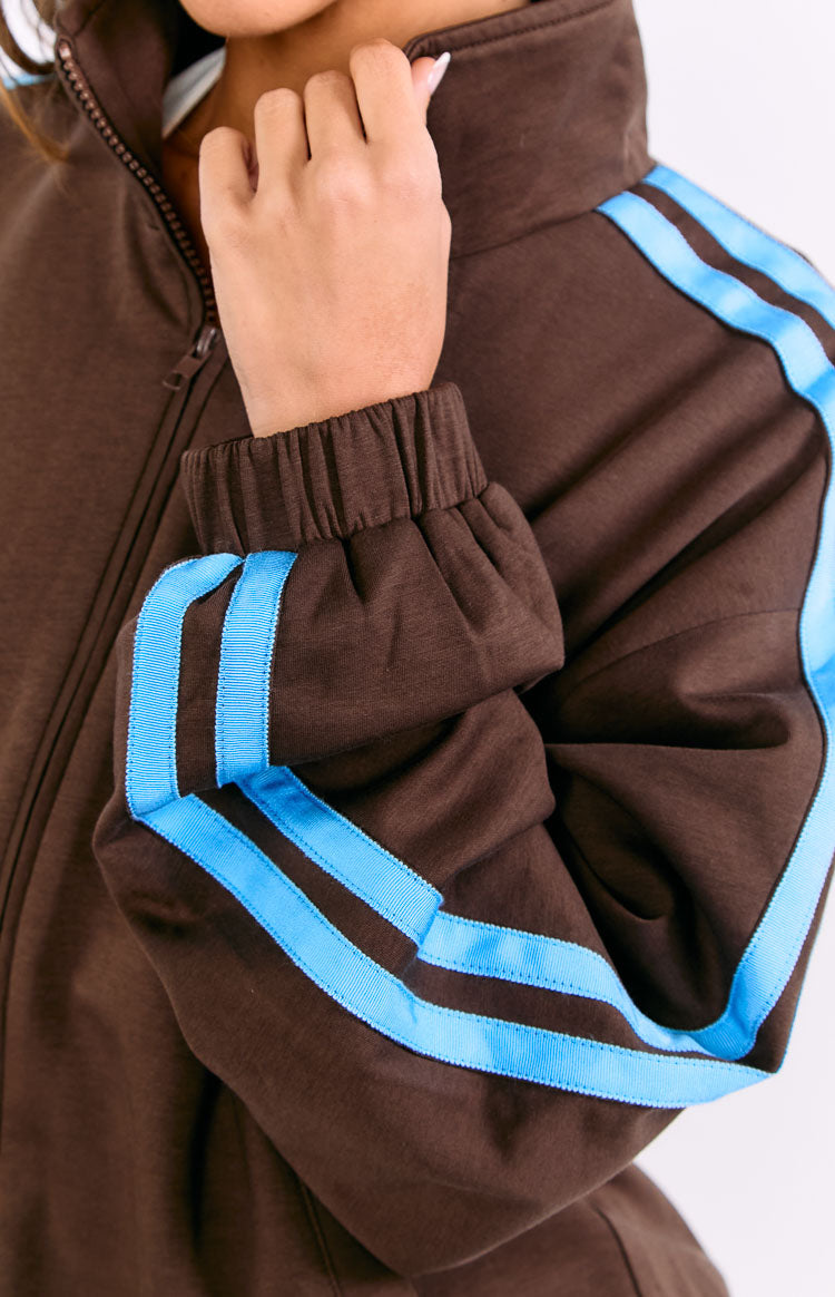 Close-up of the chocolate brown jacket's ribbed cuff, light blue sleeve stripes, and zipped stand collar