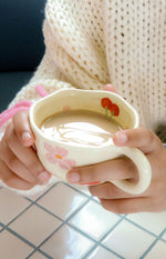 Cream mug with scalloped rim, pink flower design on the side, and red cherries on the inside rim