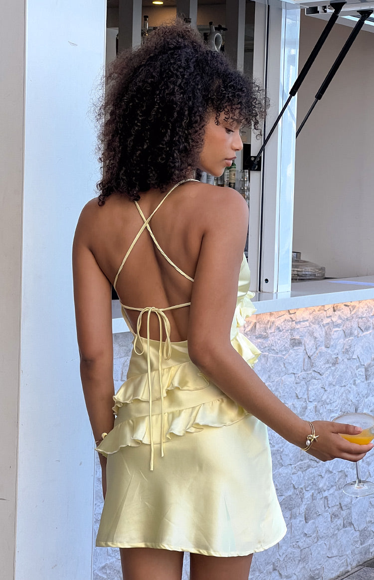 Pale yellow mini dress with a low back, criss-cross tie straps, and tiered ruffle skirt detail