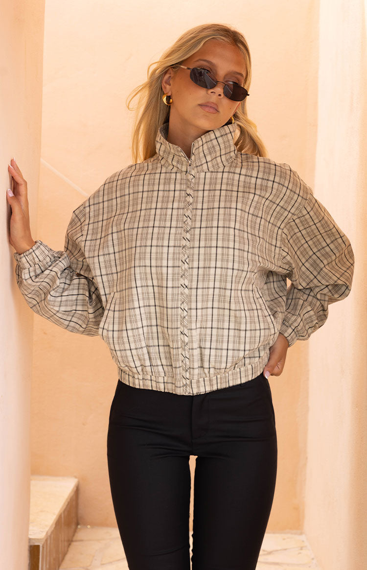 Front view of a beige plaid funnel neck jacket with a ruffled zipper and elasticated hem and cuffs