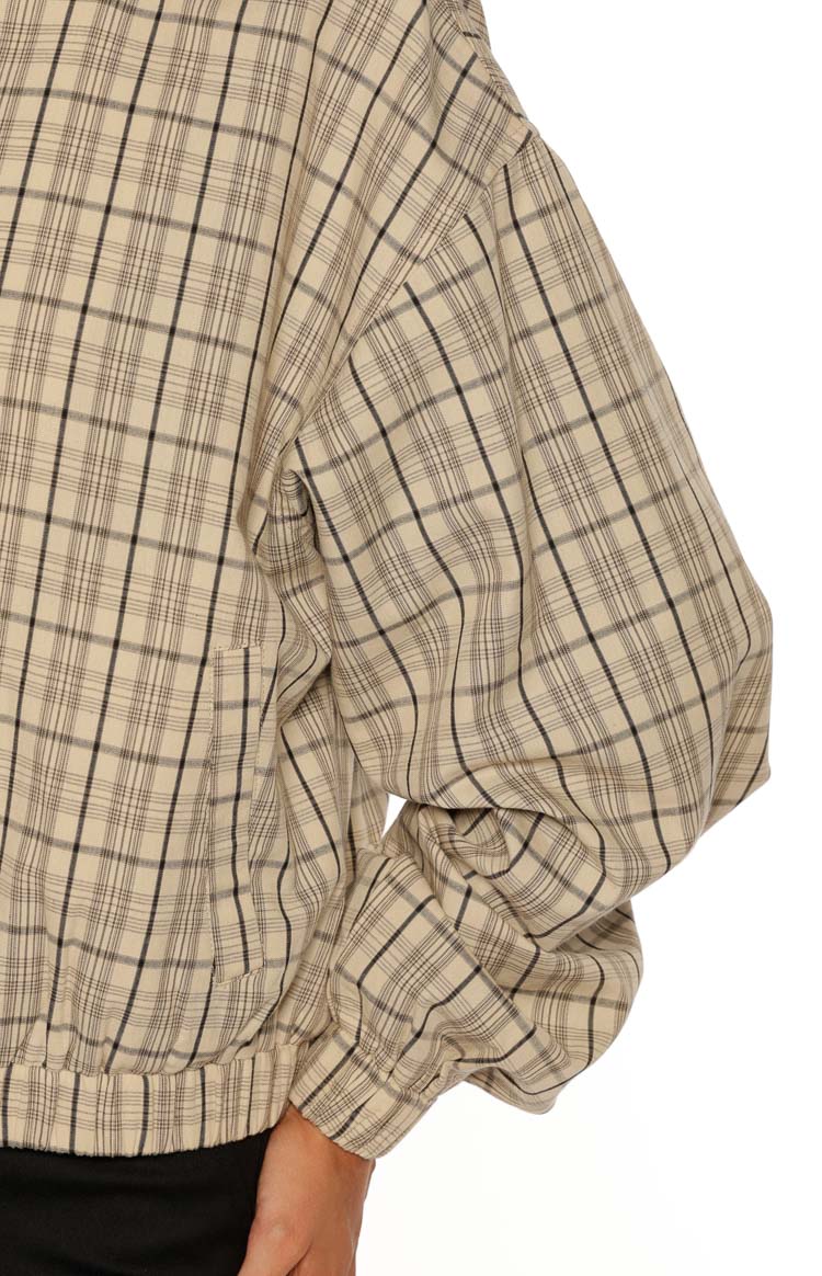Side view of the beige plaid jacket showing the long sleeve, elasticated cuff, and gathered hem