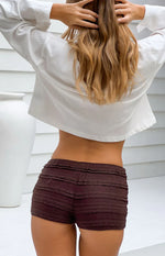 Rear view of chocolate micro shorts with horizontal ruffled tiers and lace trim