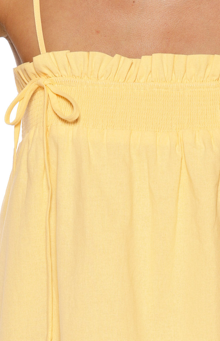 Close-up of the yellow shirred bust detail with a ruffled top edge and decorative tie on a mini dress