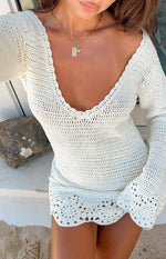 Close-up of the white crochet mini dress showing the deep V-neckline with scalloped trim and patterned hem