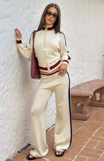 Front view of a cream knit jacquard zip sweater with a high collar, red and white striped trim, and navy sleeve stripes