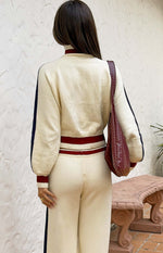 Rear view of a cream knit sweater with navy sleeve stripes, maroon trim on collar, cuffs, and double-striped hem, with matchi