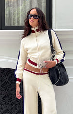 Cropped cream knit zip sweater with high collar, red and white striped cuffs and hem, and navy raglan sleeve stripes