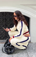 Side view of a cream knit zip sweater with cable jacquard texture, navy and burgundy sleeve stripes, and a cropped hem