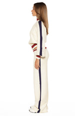Side view of a cream knit sweater with a red and navy striped ribbed collar, cuffs, hem, and a navy stripe down the sleeve