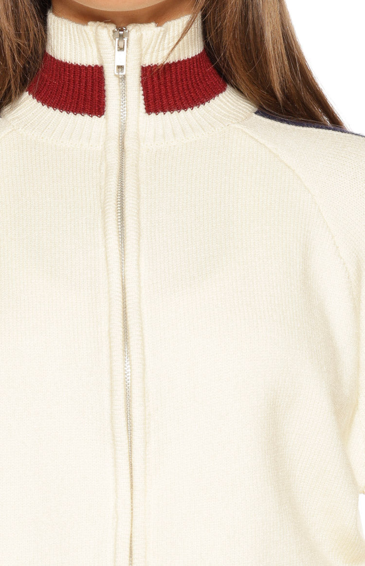 Close-up of the cream knit zip sweater showing the silver full-zip and ribbed stand collar with red and navy stripes