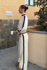 Side view of a cream knit zip sweater with a high collar, navy stripe down the arm, and burgundy trim