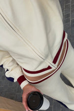 Cream knit zip sweater with ribbed hem, burgundy and brown stripes, and a waist cutout