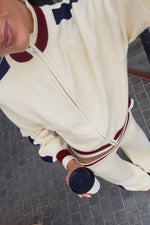 Overhead view of a cream knit zip sweater with ribbed collar, cuffs, and hem featuring navy and maroon stripes
