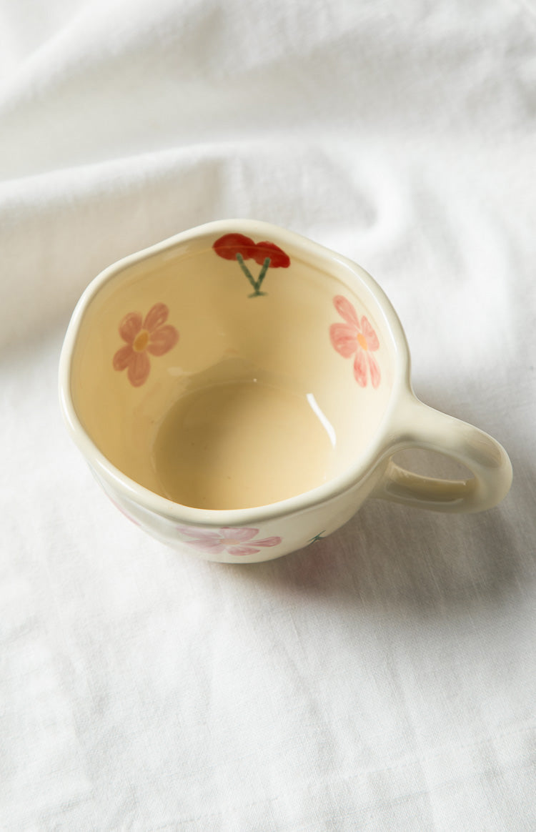 Cream ceramic mug with a pink flower and red cherry design on the side, showing the handle