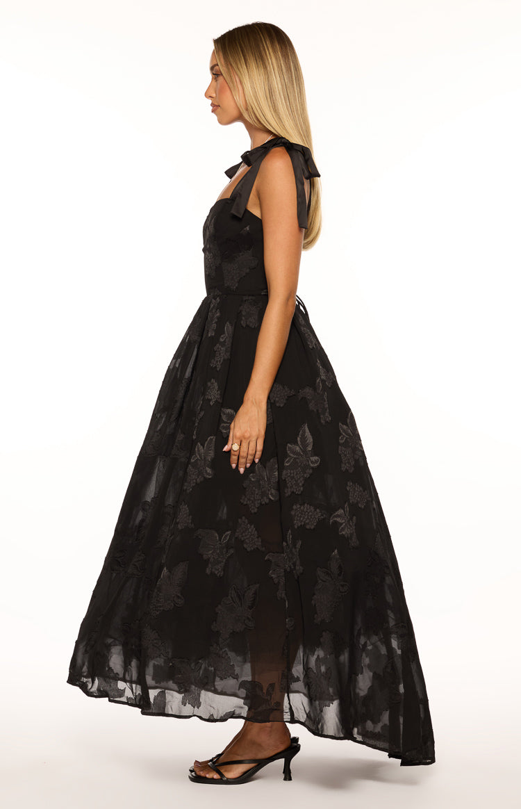 Side view of a black formal maxi dress with tie shoulders and a full skirt featuring a subtle floral texture