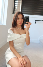 Close-up of the white off-shoulder mini dress showing the large bow detail at the bust