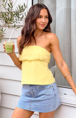 Sheer yellow strapless top with a gathered elasticated waist, flowy peplum hem, and side zipper