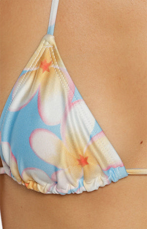 Close-up of our triangle bikini top featuring a light blue background printed with large bright white and yellow plumeria flowers. This top has thin multicolored string ties that fasten around the neck and back.
