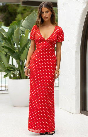 Our model wears a long maxi-length dress in a vibrant red fabric with an all-over print of small white polka dots features a plunging V-neckline a fitted bodice with subtle gathering at the bust and short slightly puffed sleeves. This maxi is long and flowing.