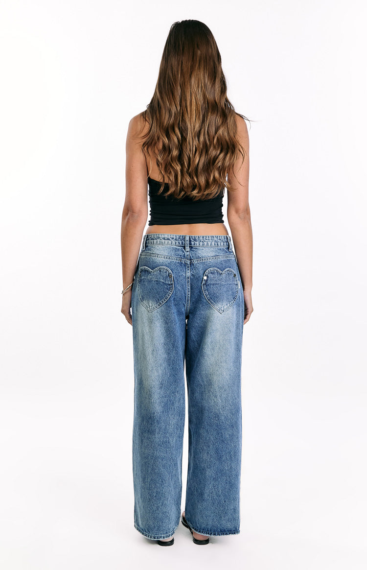 Rear view of mid wash denim slouchy jeans with unique heart-shaped back pockets and a relaxed wide-leg fit