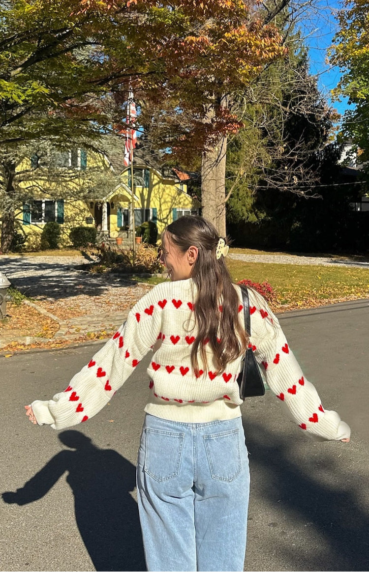 Front view of a white knitted jumper with red heart patterns, long sleeves, and a relaxed fit