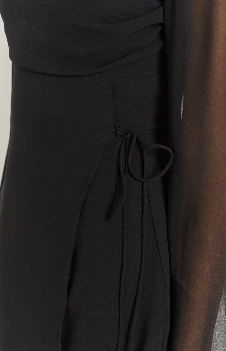 Side view of a black mini dress with sheer long sleeves and a flowy skirt with a sheer hem