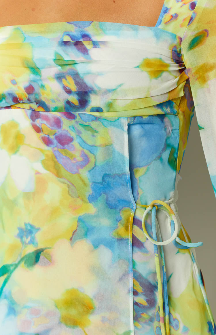 Side view of a blue floral long sleeve mini dress with ruched side seams and flared cuffs