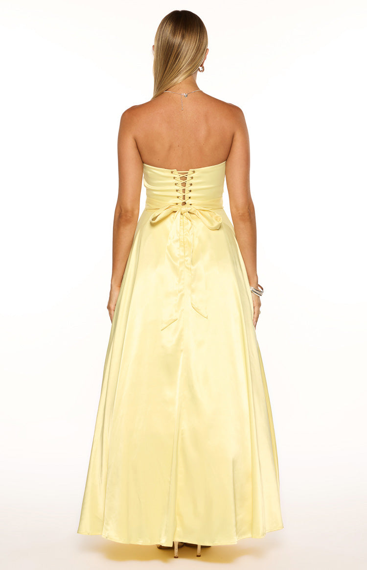 Side view of a yellow satin strapless maxi dress with a fitted waist and a tie detail at the back