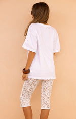 Rear view of white floral lace mid rise capri pants with a delicate pattern and small hem slits