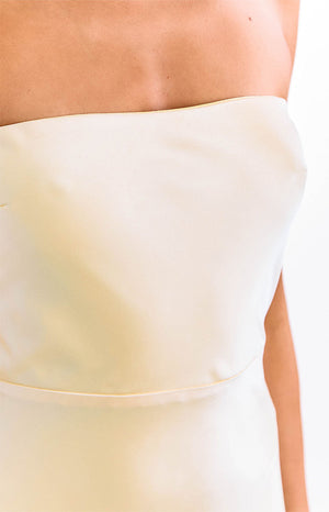 A model in a yellow strapless maxi dress with an elegant straight neckline. This sophisticated formal dress features a sleek column silhouette. An ideal choice for a wedding guest or graduation ceremony.