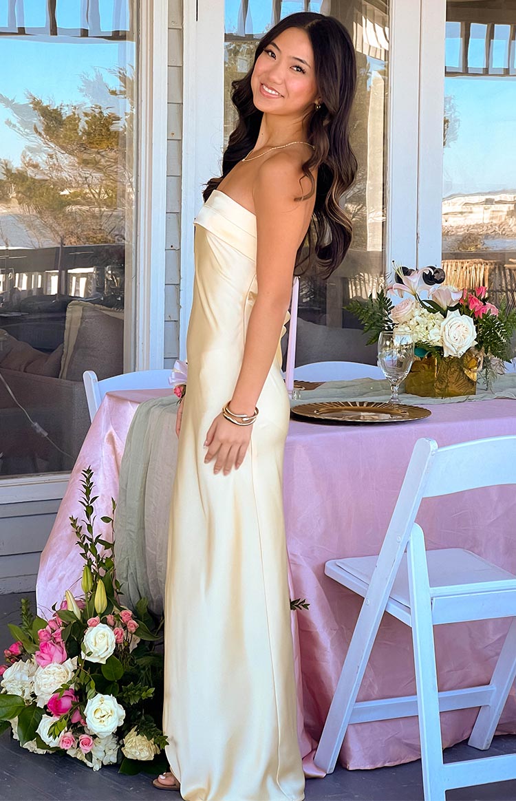 Side view of a yellow strapless satin maxi dress with a fitted bodice and flowing skirt