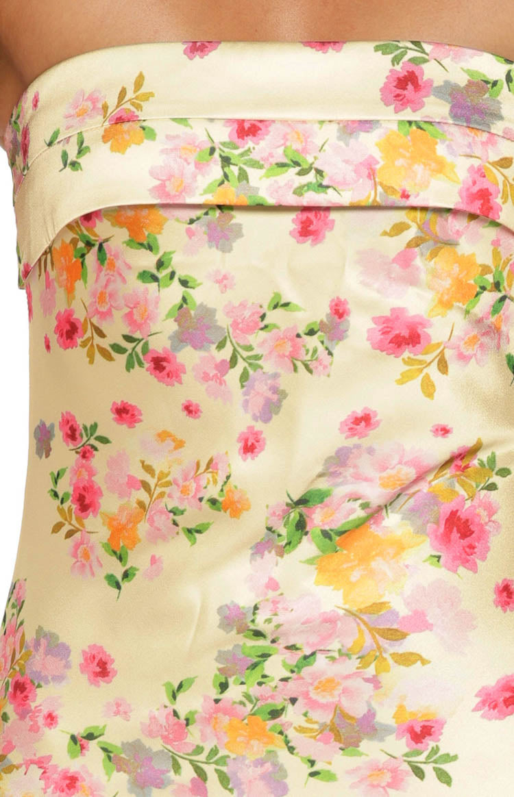 Close-up of the banded strapless neckline and yellow satin floral print of a maxi dress